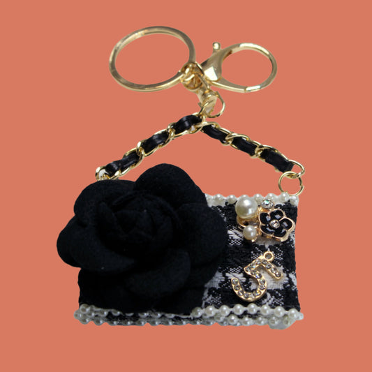 Black handbag keychain with flower and pearl details on a white background
