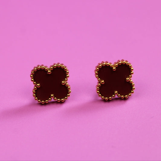 Gold earrings with a clover design on a pink background