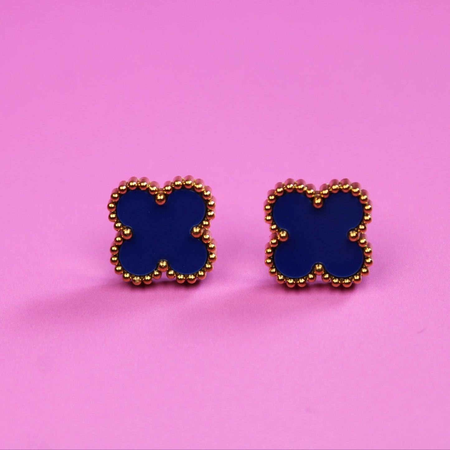 Butterfly-shaped earrings with blue centers and gold borders on a pink background