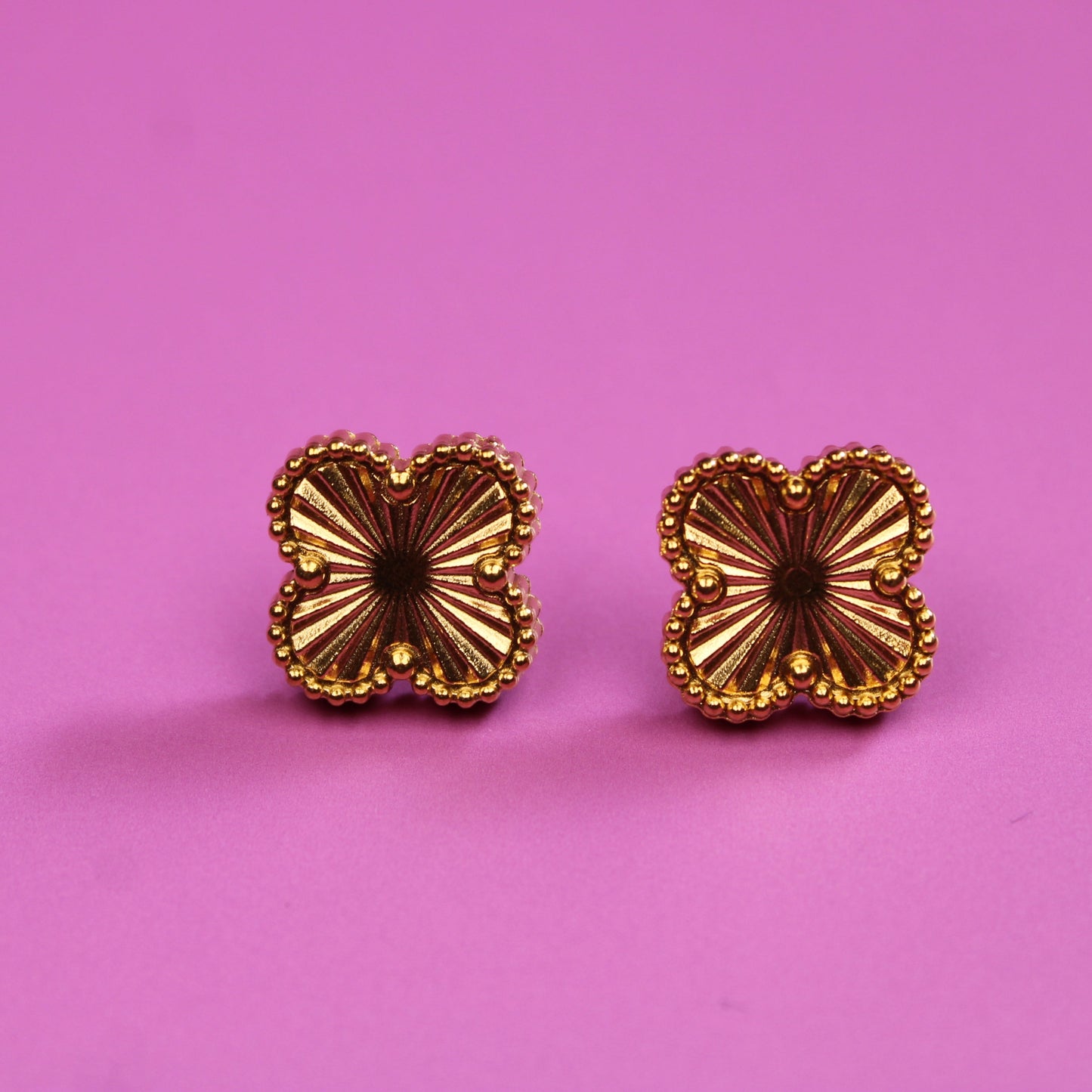 Gold butterfly-shaped earrings on a pink background