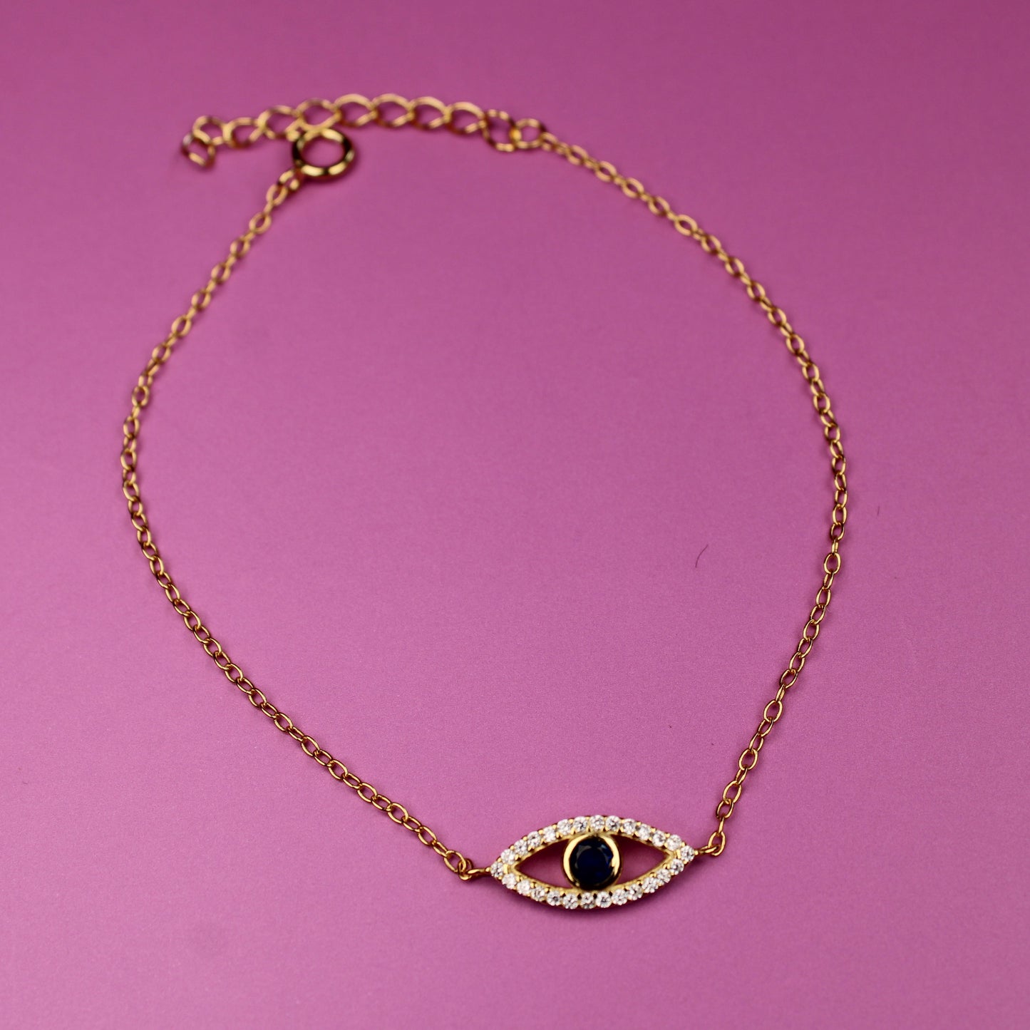 Gold bracelet with an eye-shaped charm on a pink background