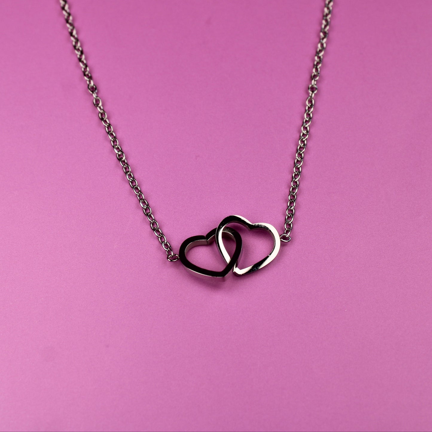 Necklace with interlocking heart pendants on a pink background