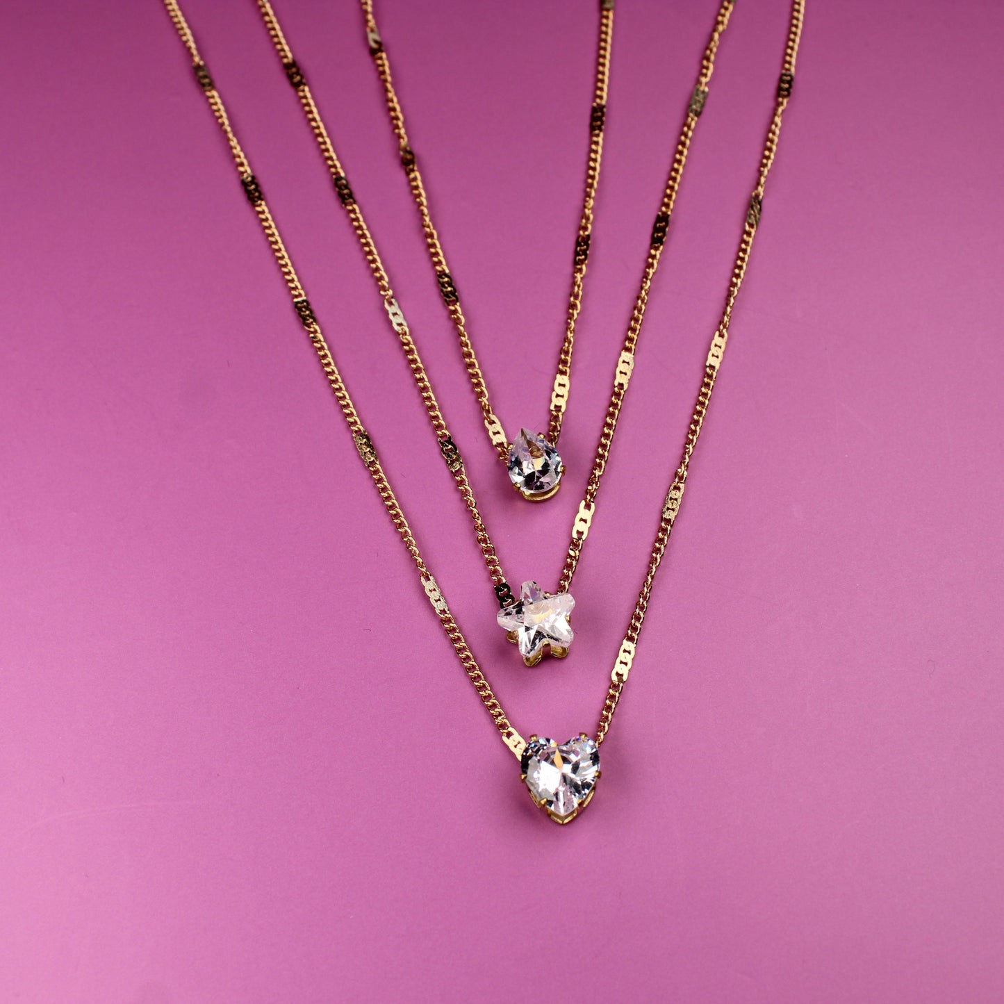 Three gold necklaces with star pendants on a pink background