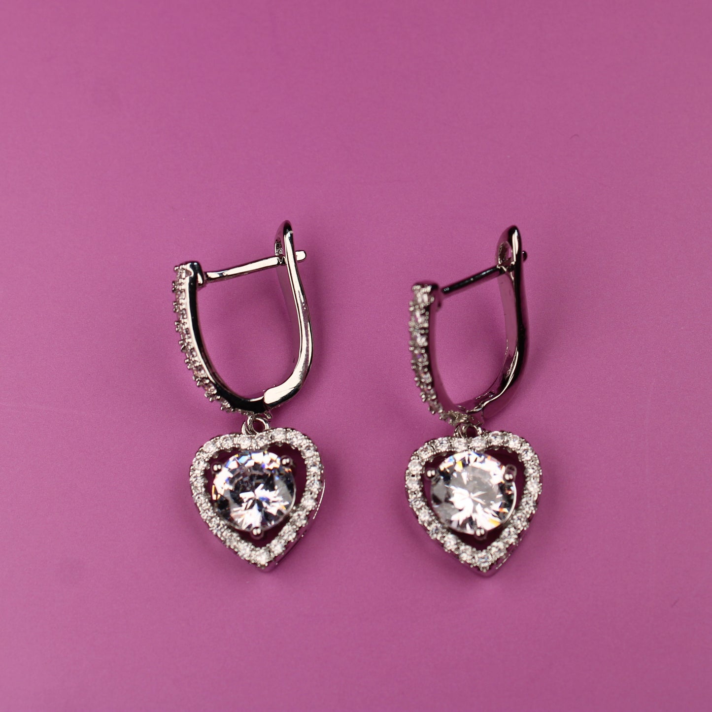 Heart-shaped earrings with clear stones on a pink background