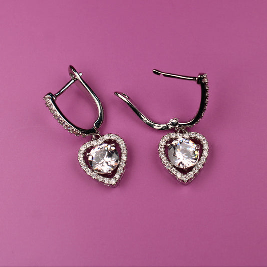 Heart-shaped earrings with clear stones on a pink background