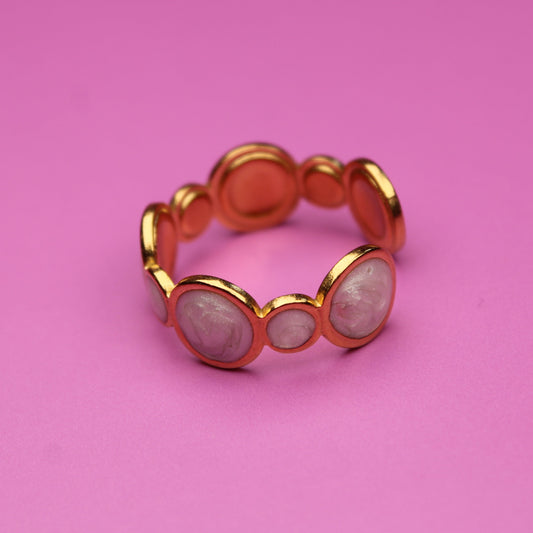 Gold ring with circular design on a pink background