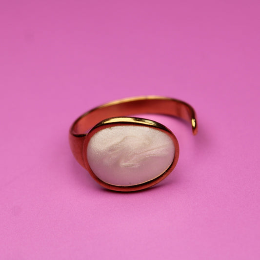 Gold ring with a white stone on a pink background