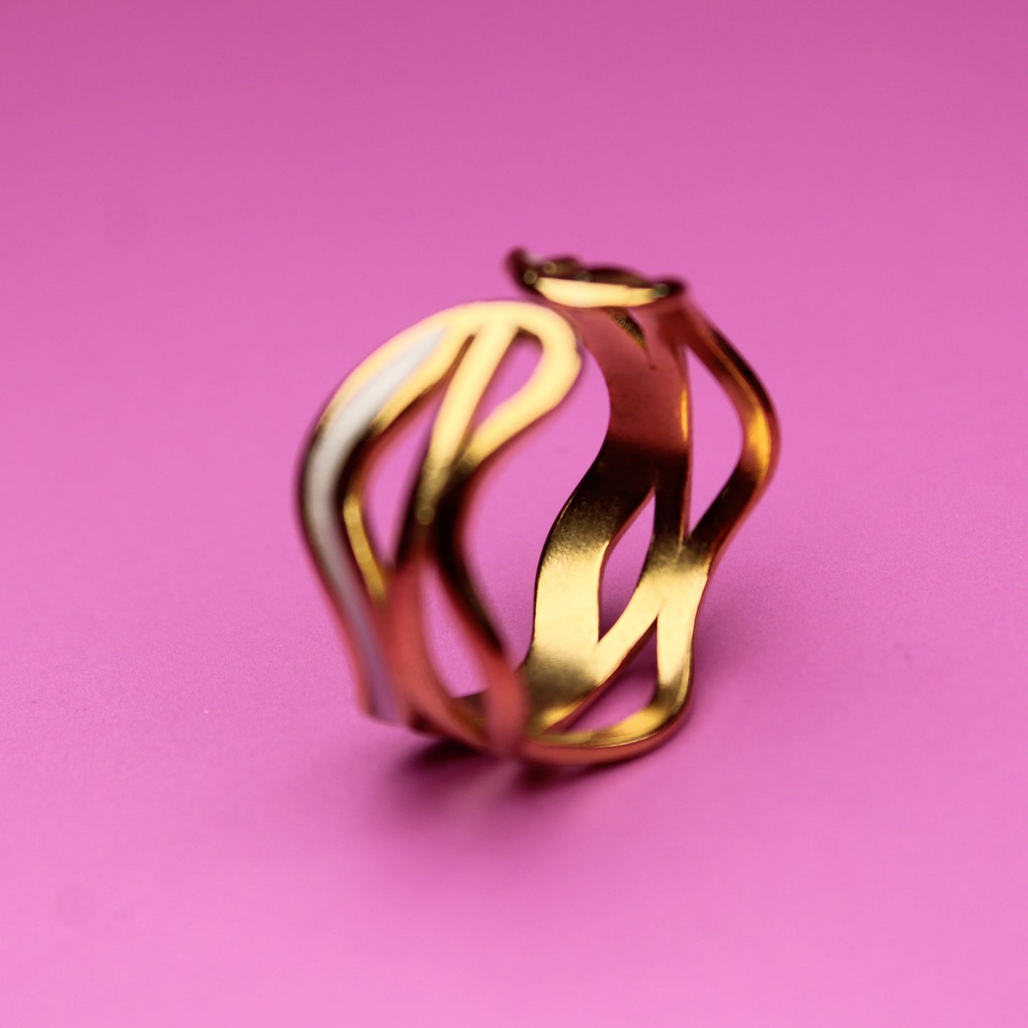 Gold ring with wavy design on a pink background