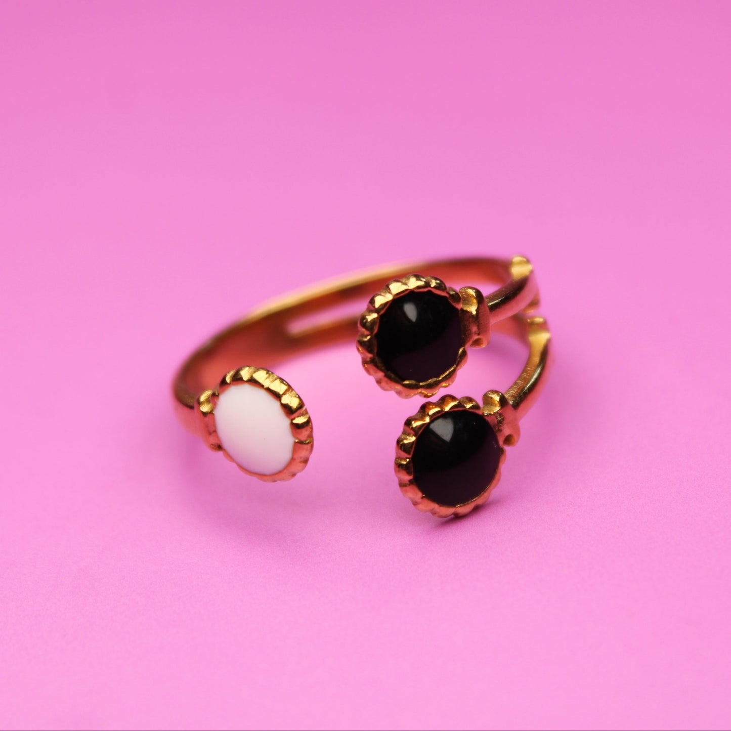 Gold ring with black and white gemstones on a pink background