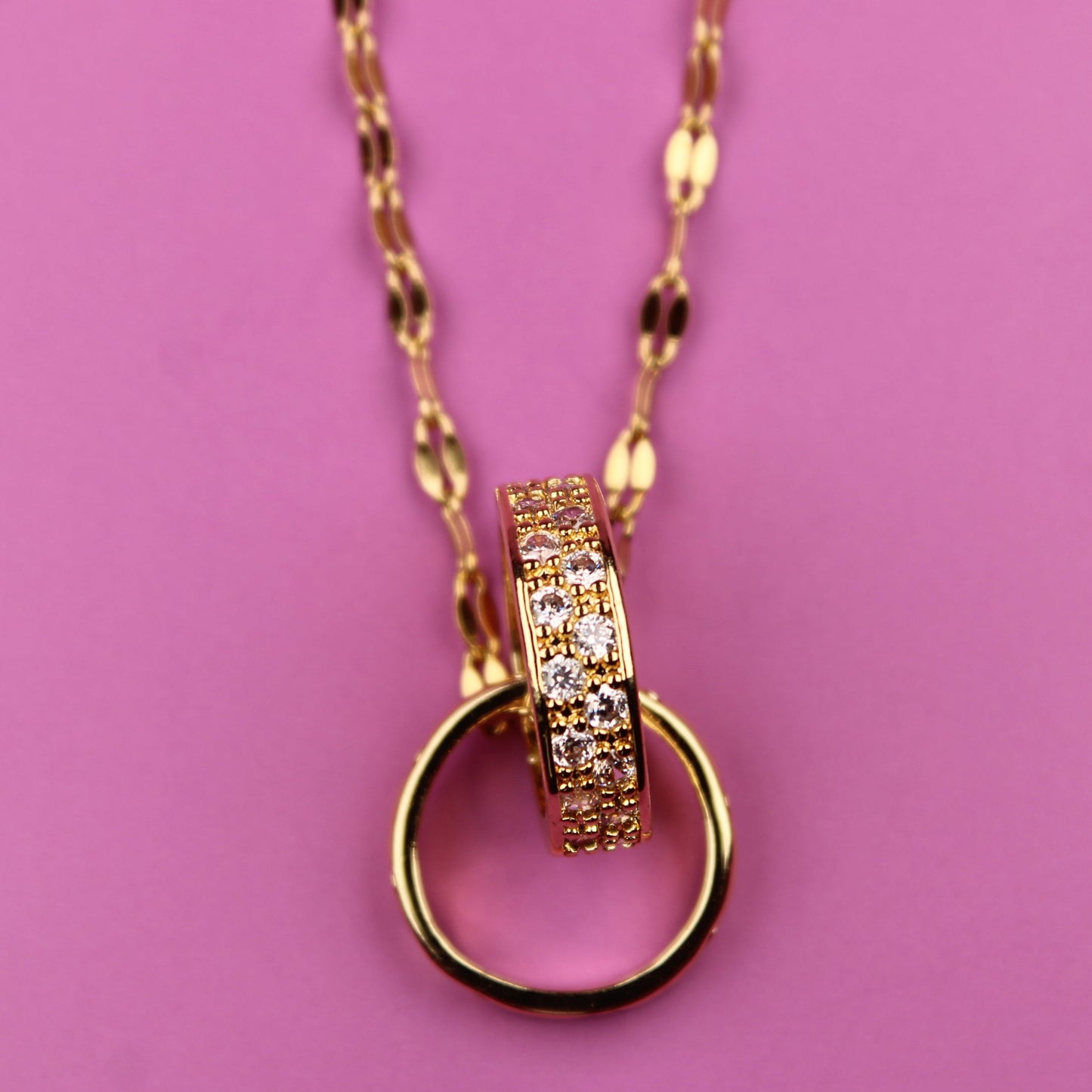Gold necklace with a ring pendant on a pink background