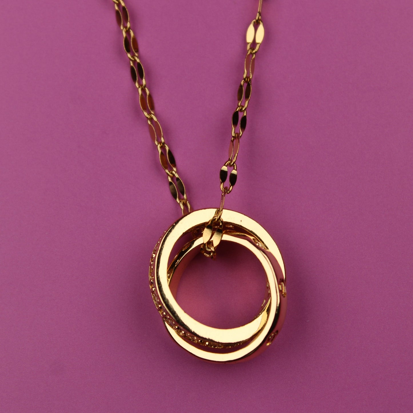 Gold necklace with a circular pendant on a purple background