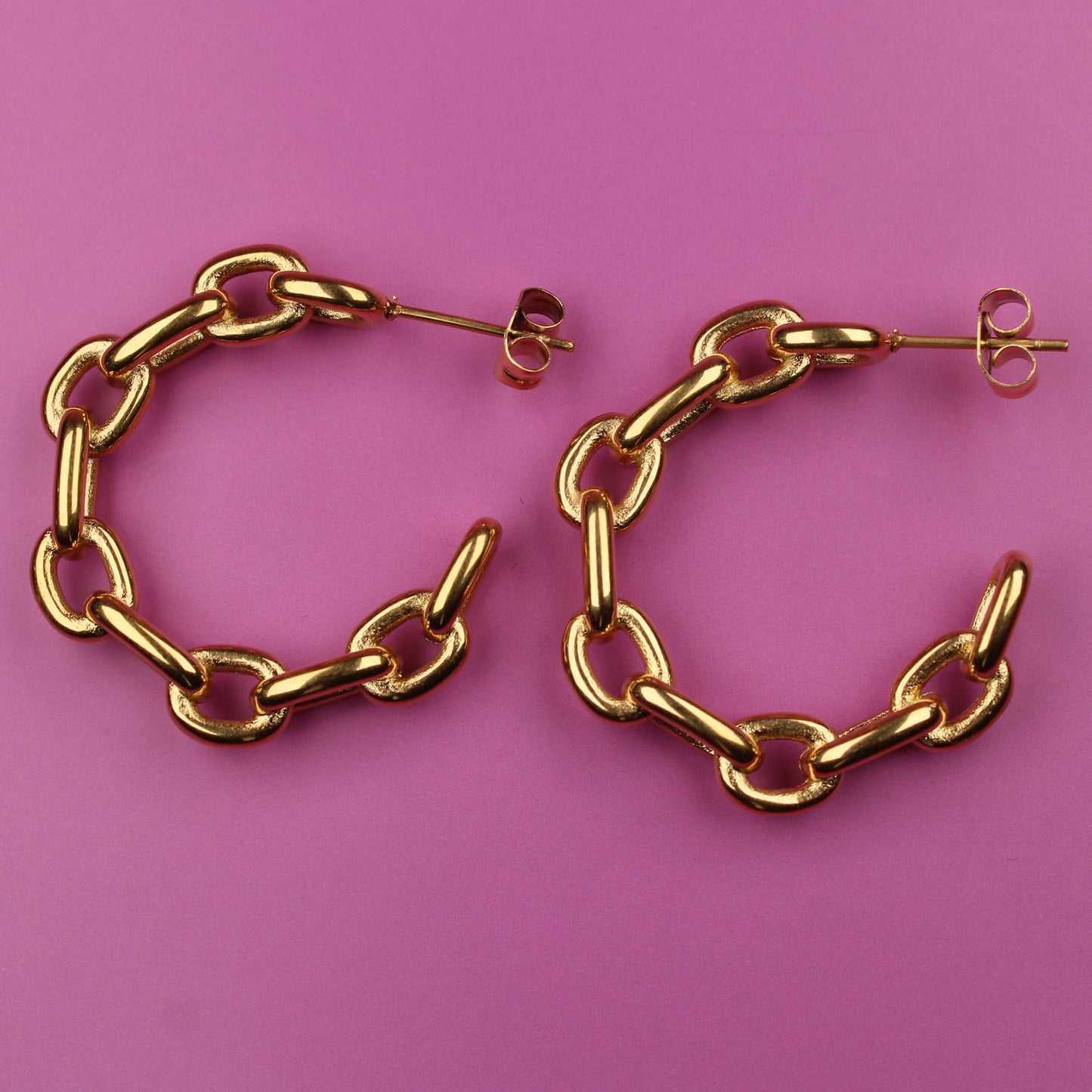 Gold chain hoop earrings on a pink background