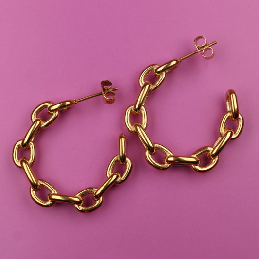 Gold chain hoop earrings on a pink background