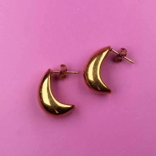 Gold moon-shaped earrings on a pink background