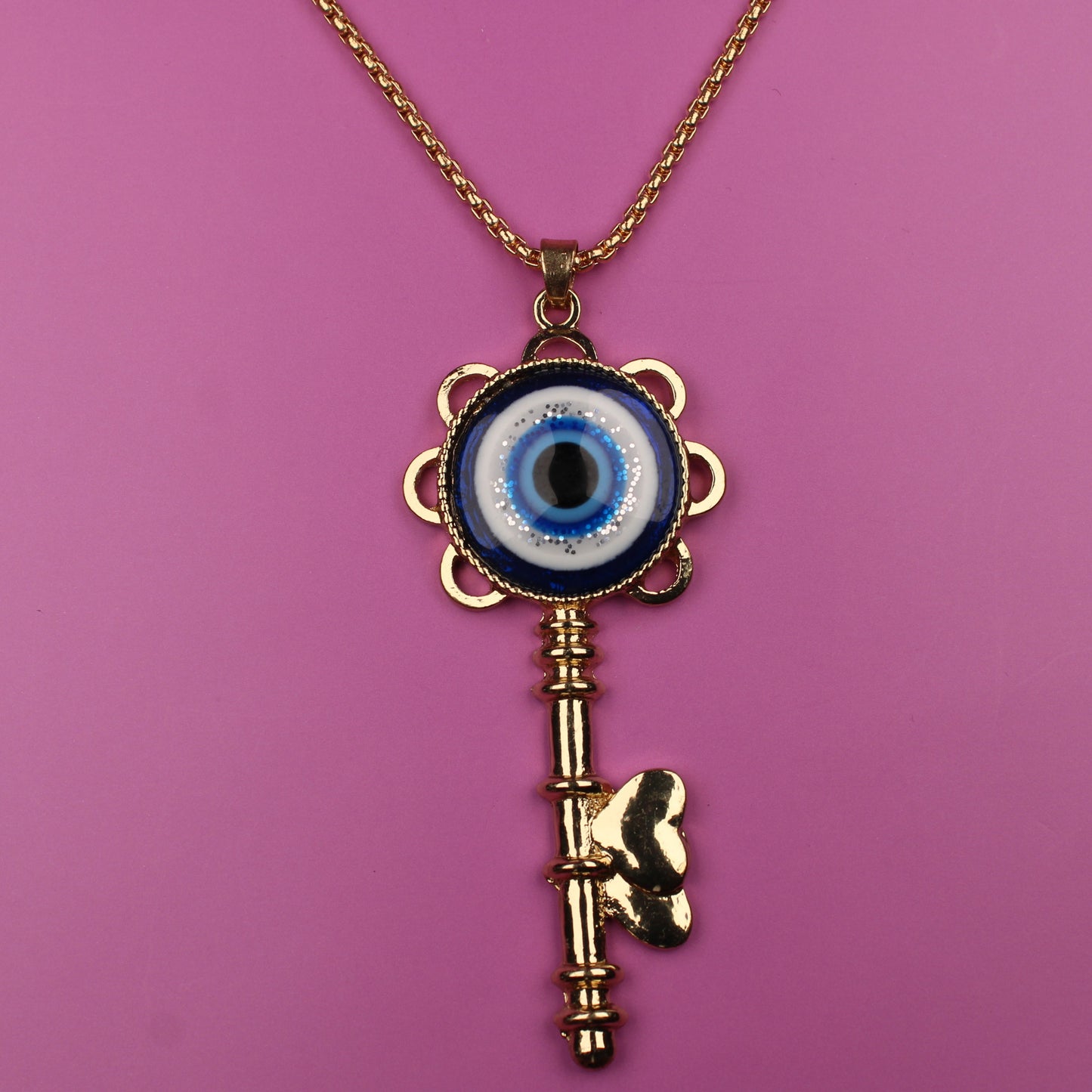 Gold key-shaped necklace with an eye pendant on a pink background