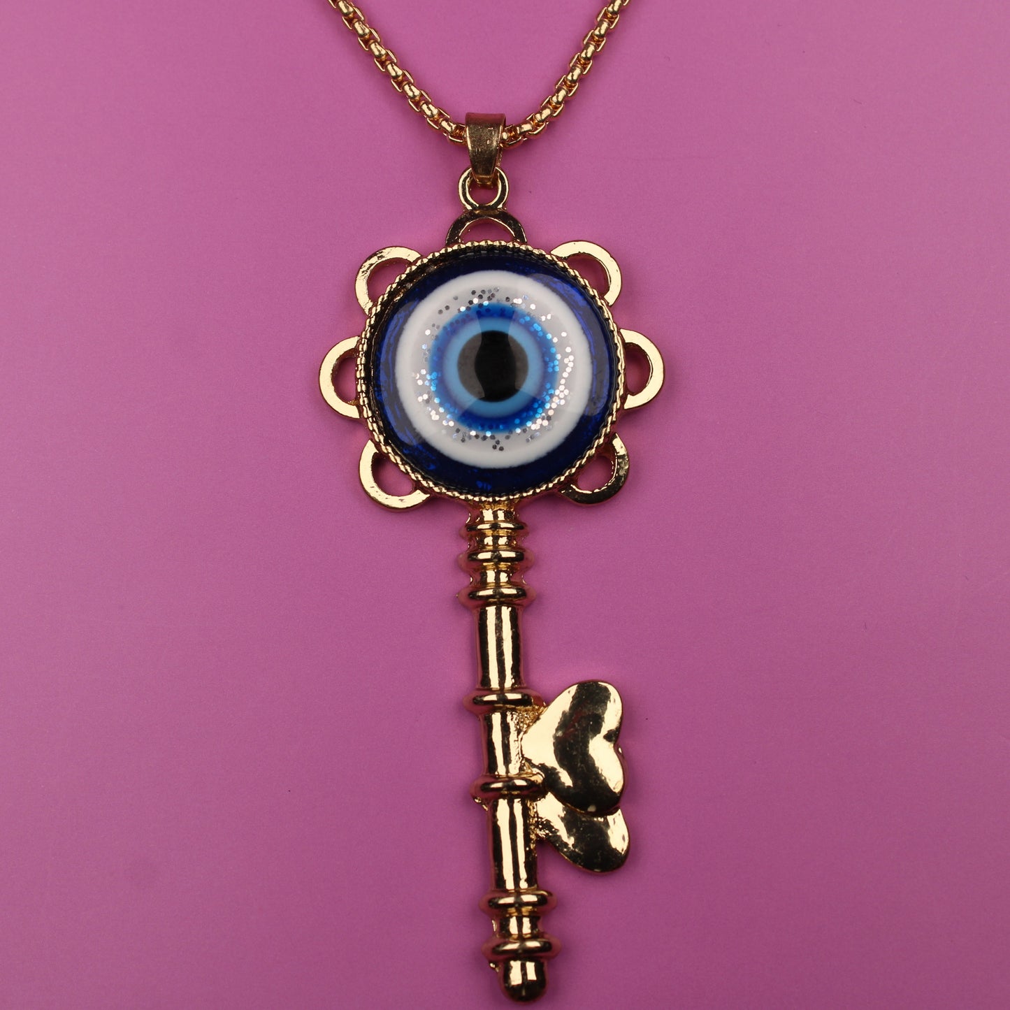 Gold key-shaped necklace with an eye design on a pink background
