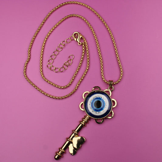 Gold key-shaped necklace with an eye pendant on a pink background
