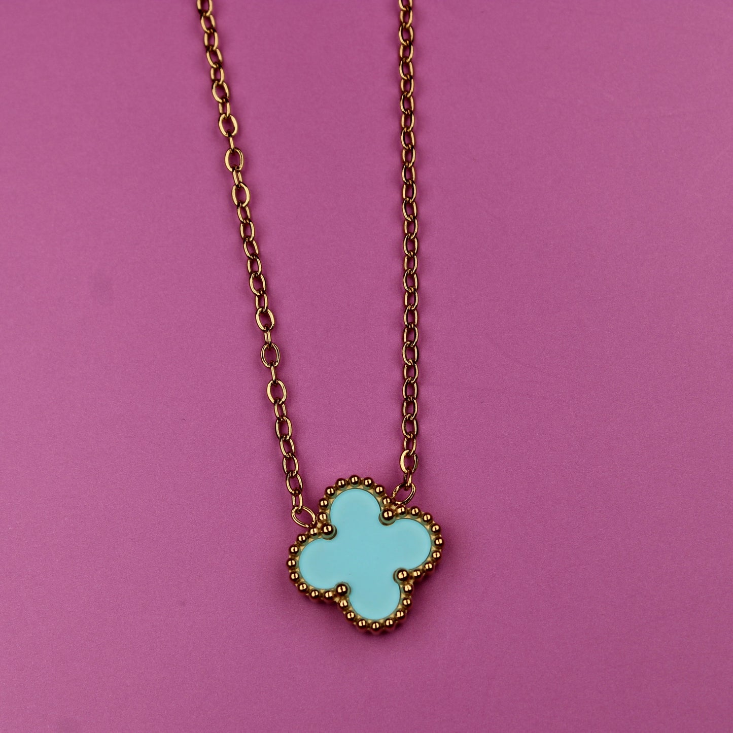 Necklace with a turquoise clover-shaped pendant on a pink background
