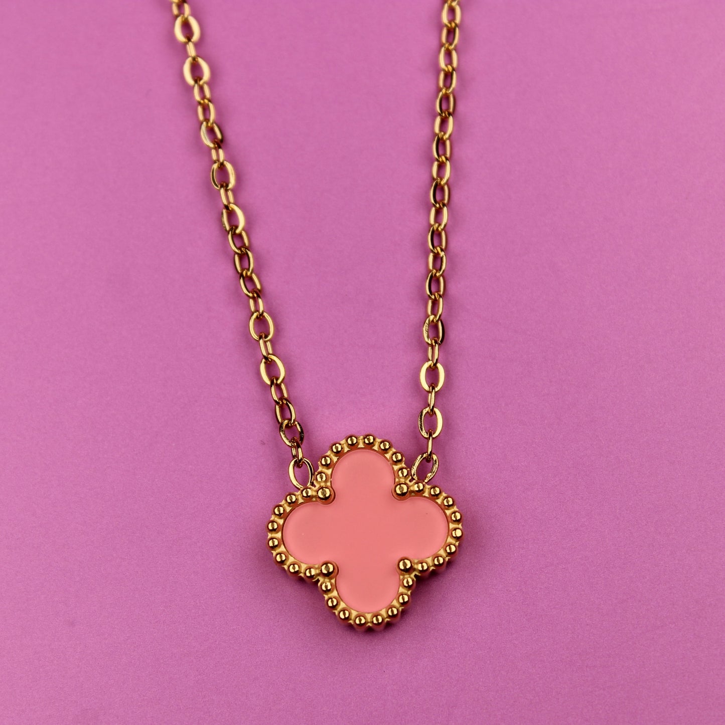 Pink clover-shaped pendant on a gold chain against a pink background
