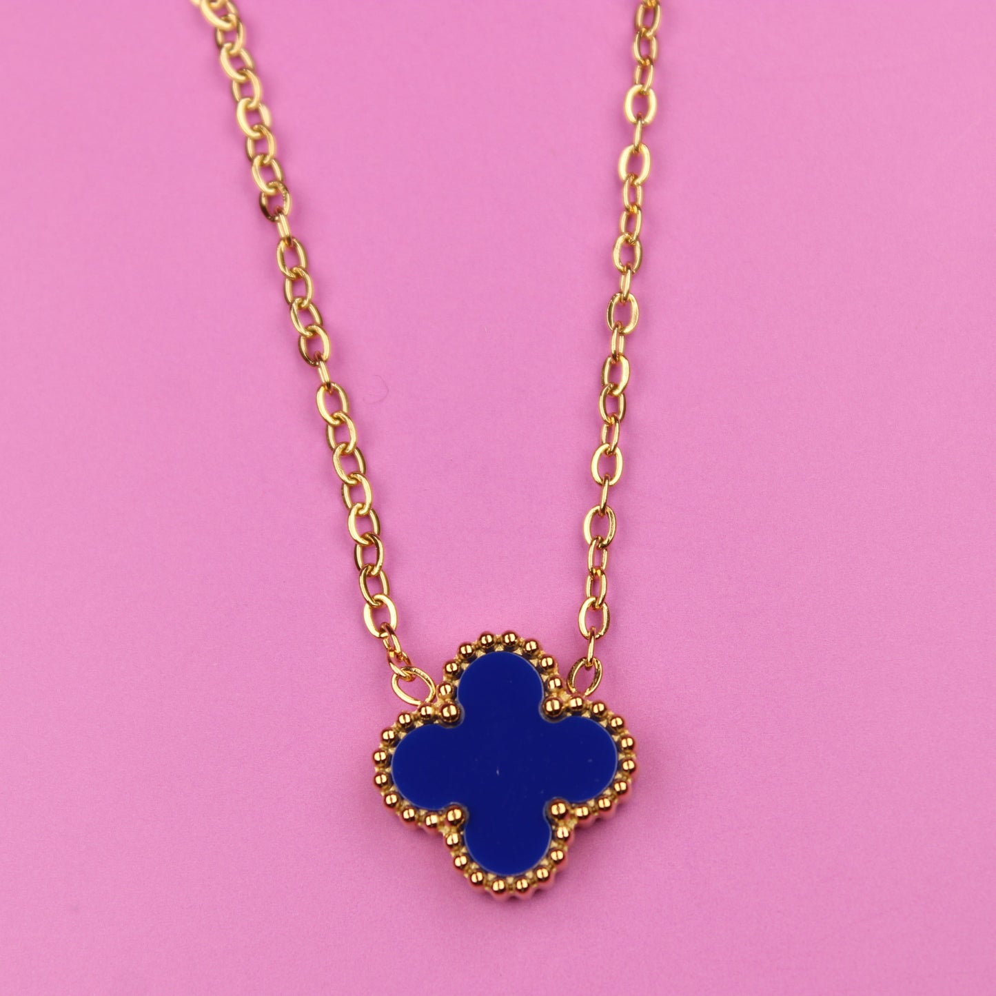 Gold necklace with a blue clover pendant on a pink background