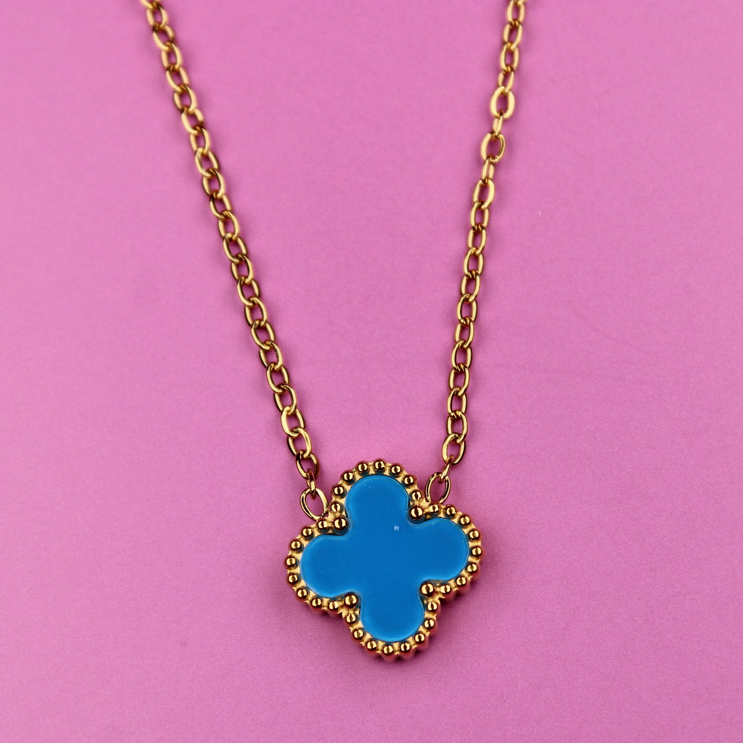 Necklace with a blue clover pendant on a pink background