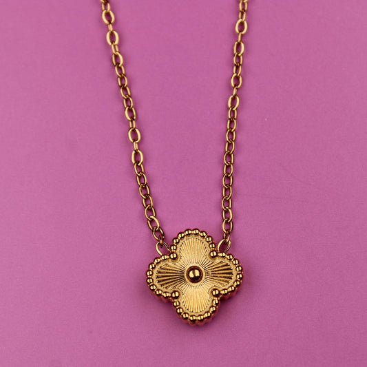 Gold necklace with a heart-shaped pendant on a pink background