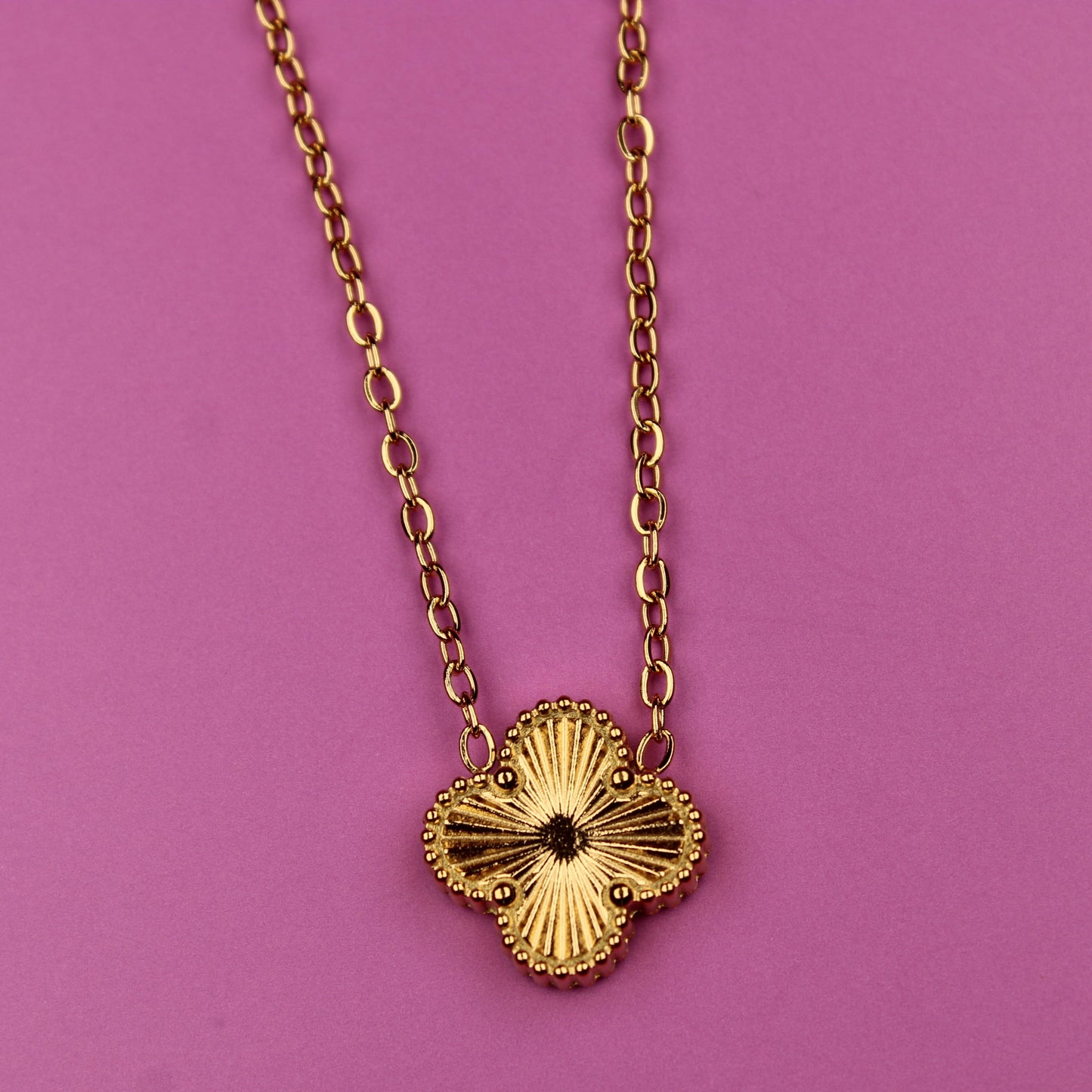 Gold necklace with a floral pendant on a pink background