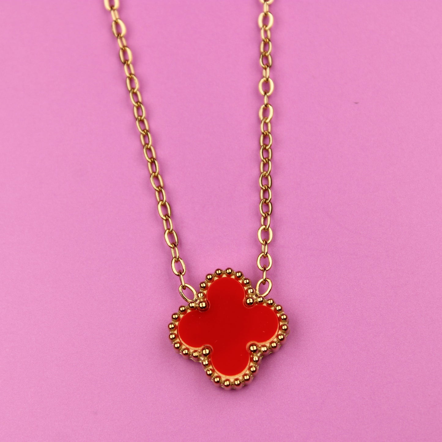 Necklace with a red clover-shaped pendant on a pink background