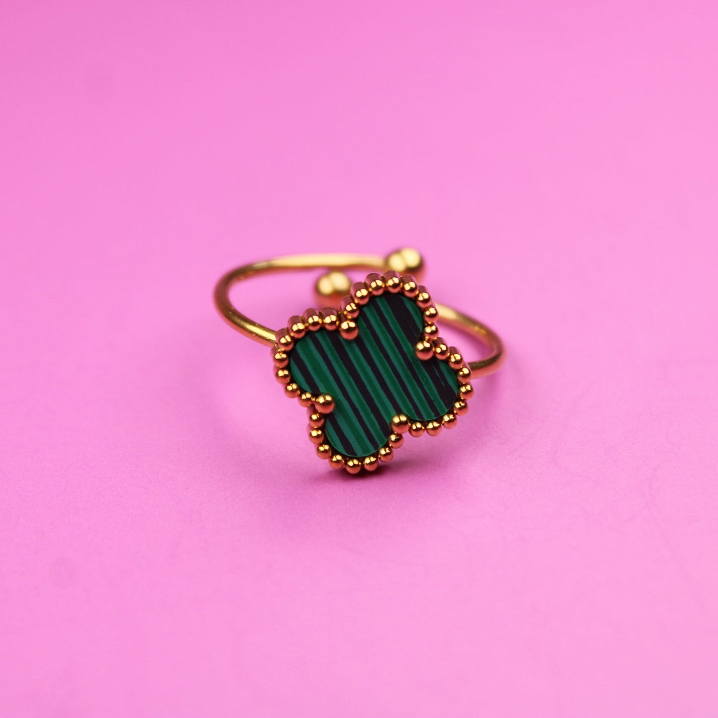 Gold ring with green gemstone on a pink background