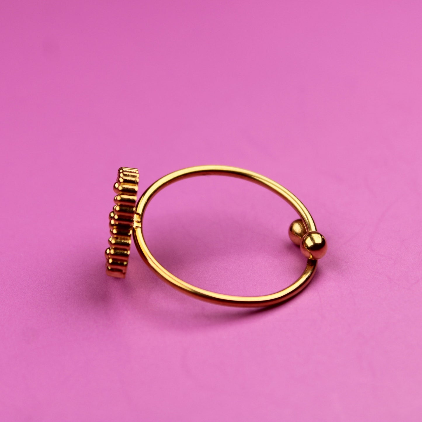 Gold ring with a small decorative element on a pink background