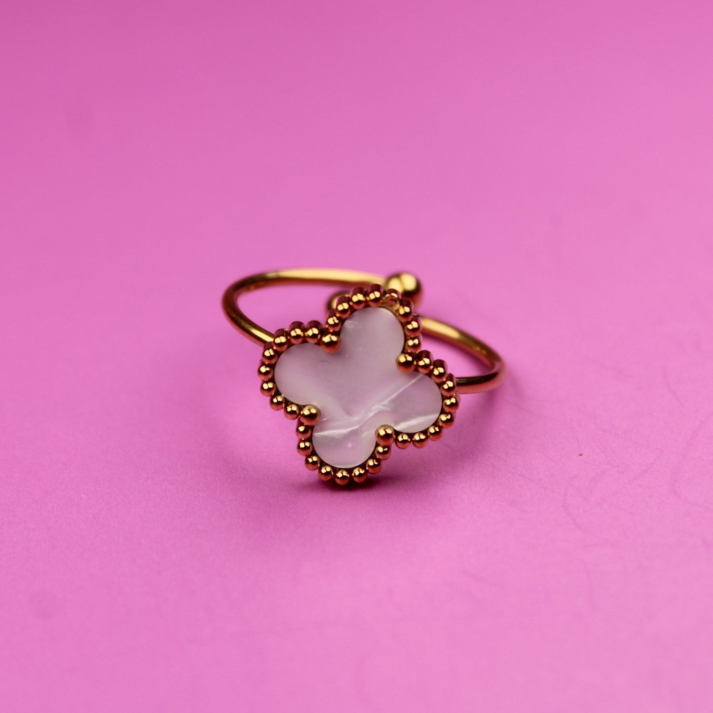 Gold ring with a white stone on a pink background