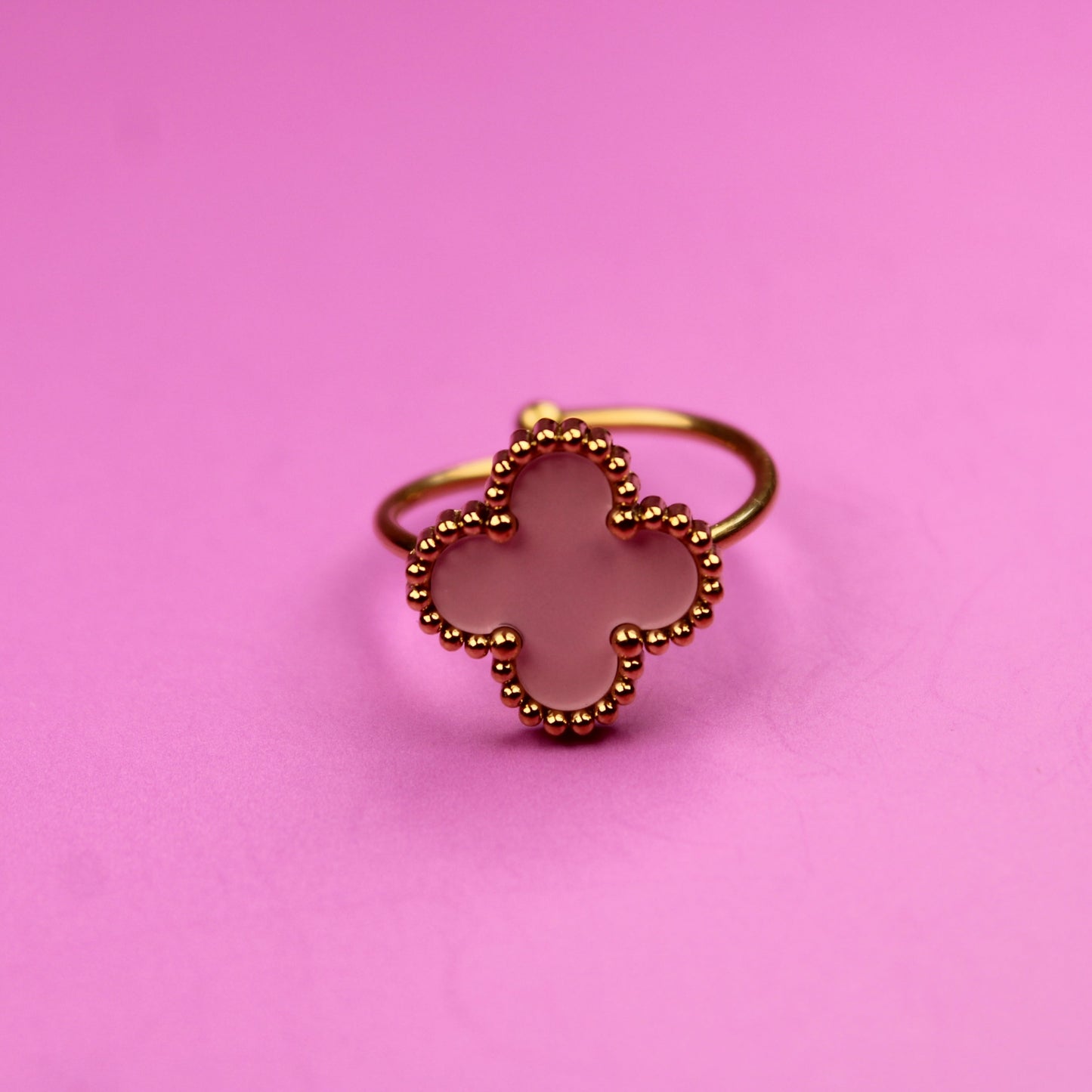 Gold ring with a clover design on a pink background