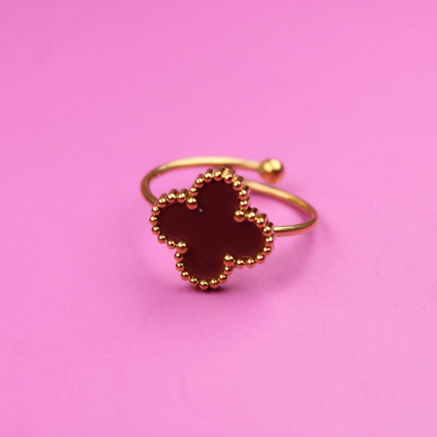 Gold ring with a clover design on a pink background