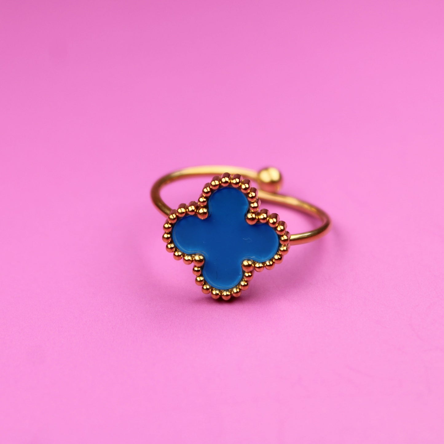 Gold ring with a blue clover-shaped stone on a pink background