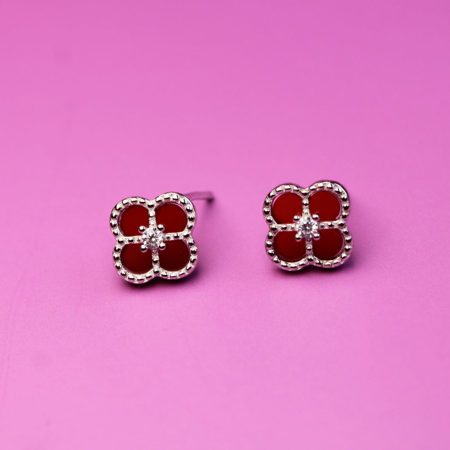 Red flower-shaped earrings on a pink background
