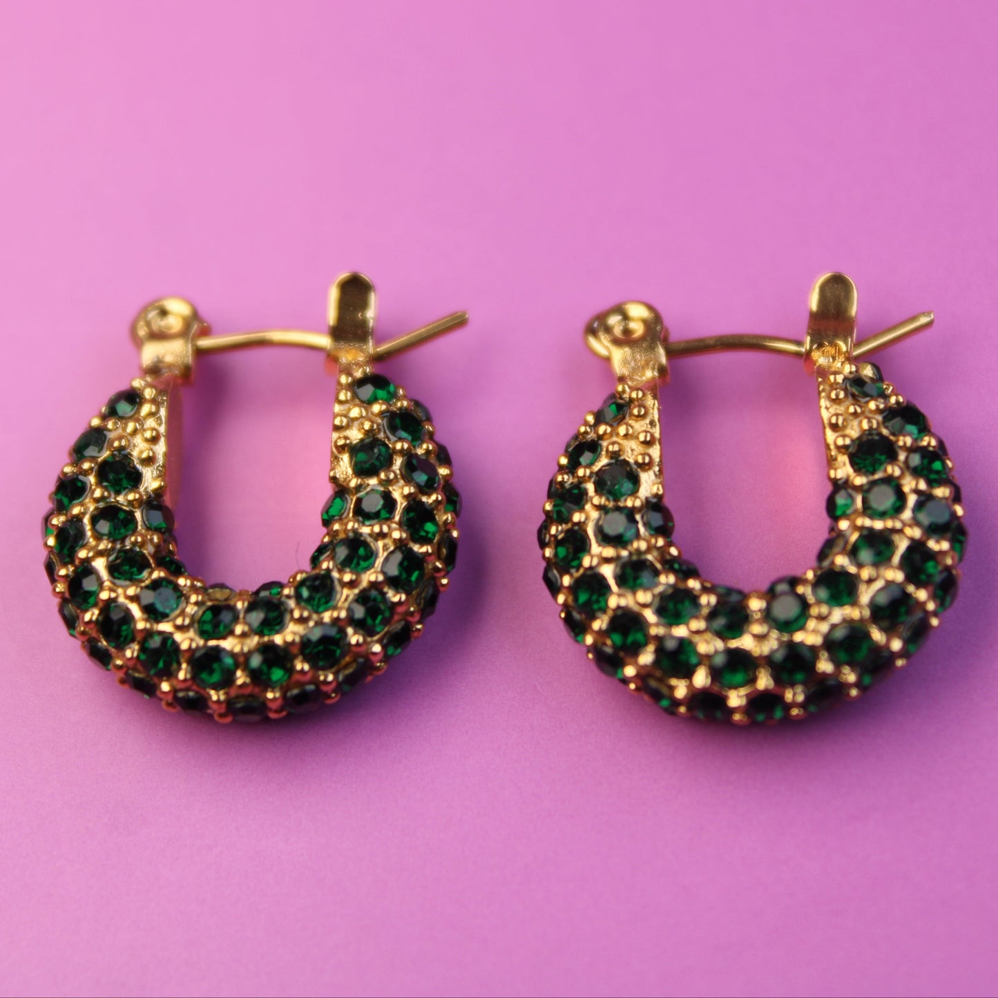 Gold hoop earrings with green gemstones on a pink background