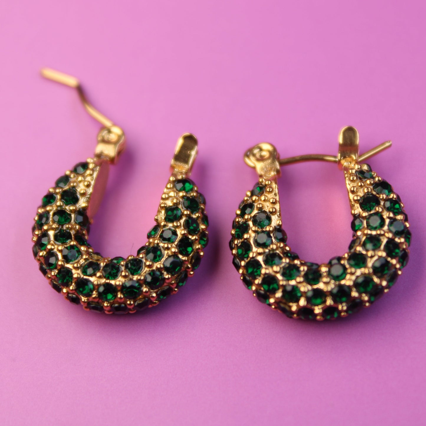 Gold hoop earrings with green gemstones on a pink background