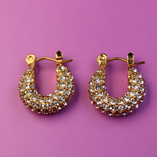 Gold hoop earrings with gemstones on a purple background