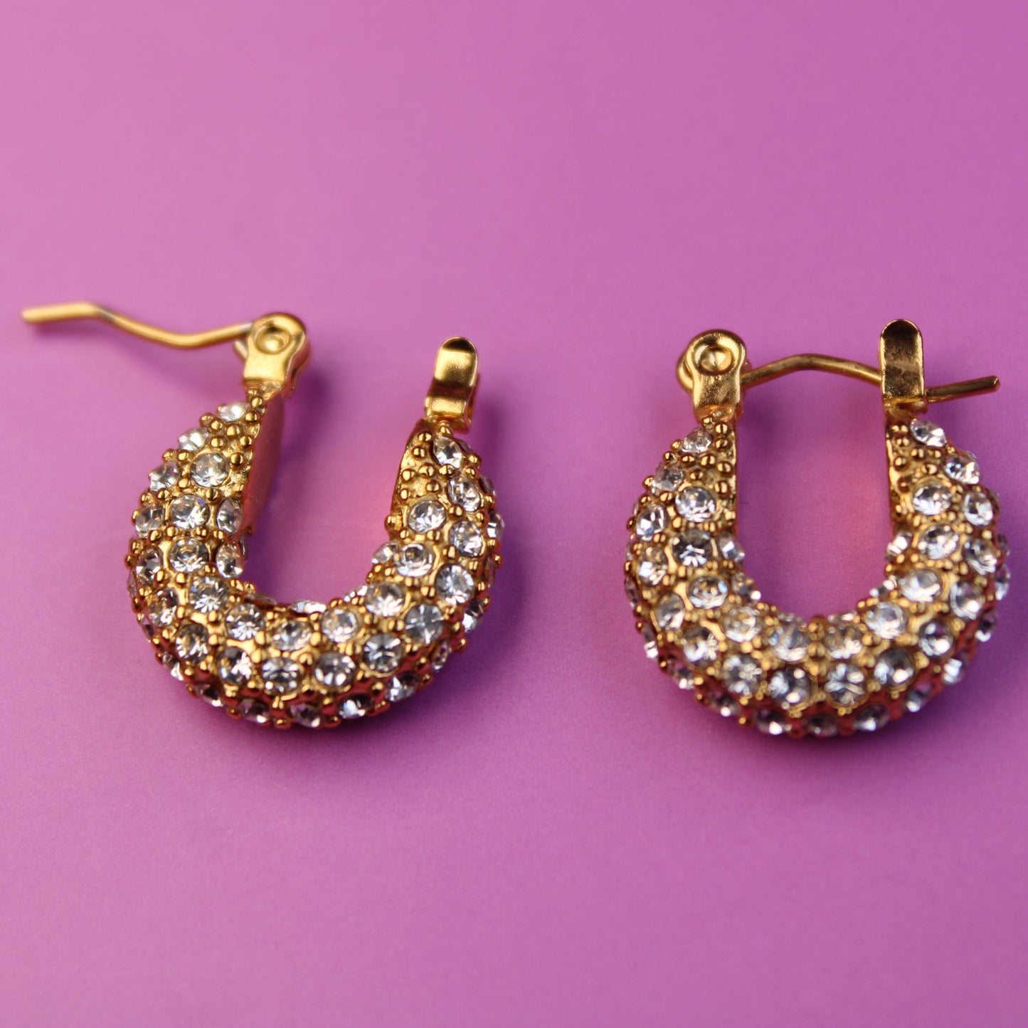 Gold hoop earrings with gemstones on a pink background