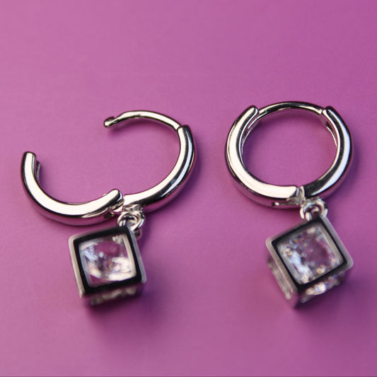 Pair of silver hoop earrings with square gemstones on a purple background