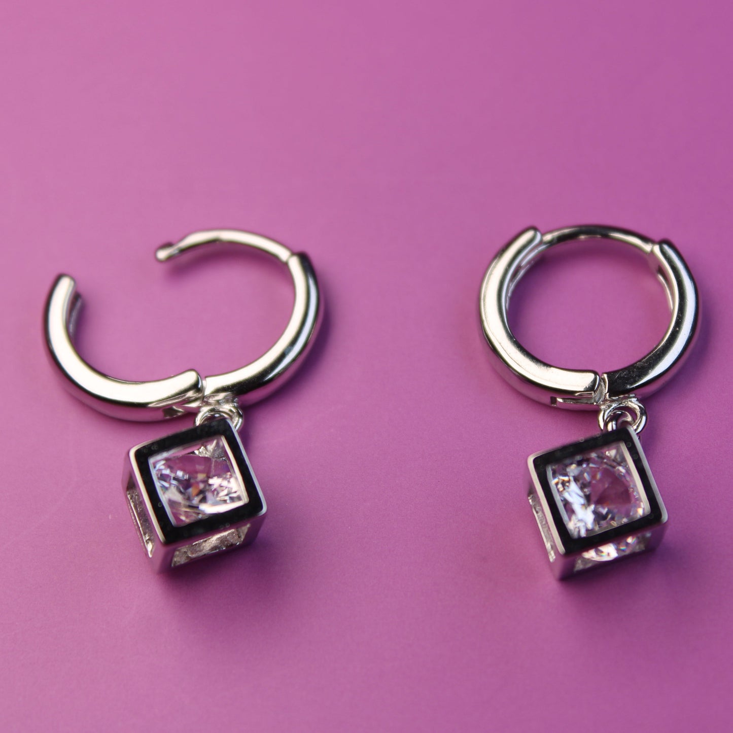 Pair of silver hoop earrings with square gemstones on a pink background