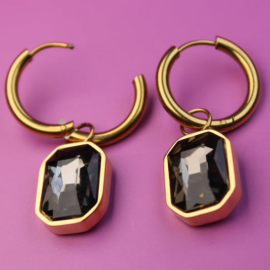 Gold hoop earrings with black gemstones on a purple background