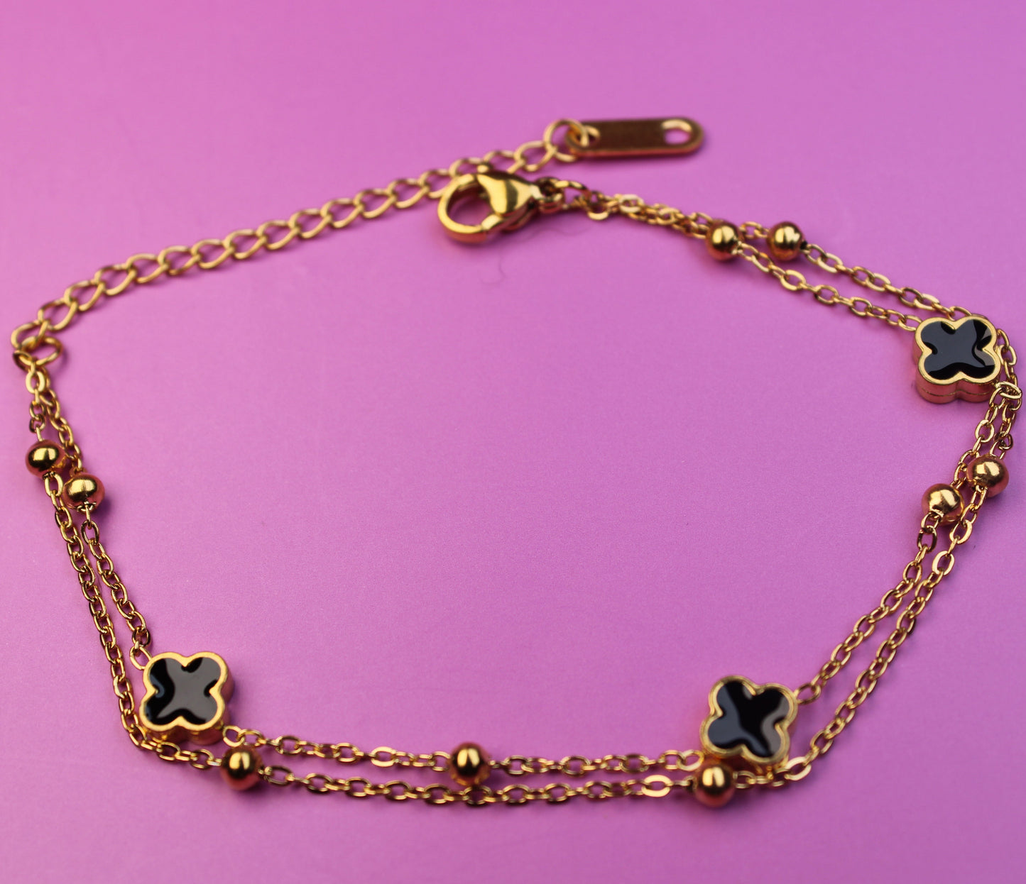 Gold bracelet with clover-shaped charms on a pink background