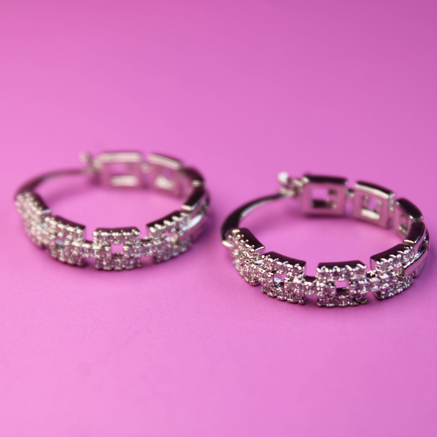 Pair of silver hoop earrings with pink gemstones on a pink background