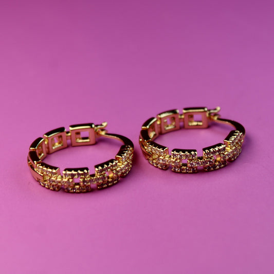 Gold hoop earrings with gemstones on a pink background