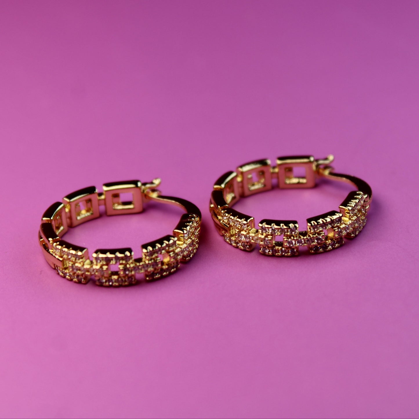 Gold hoop earrings with gemstones on a pink background