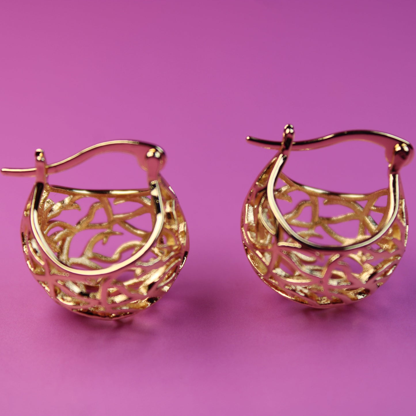 Gold hoop earrings on a pink background