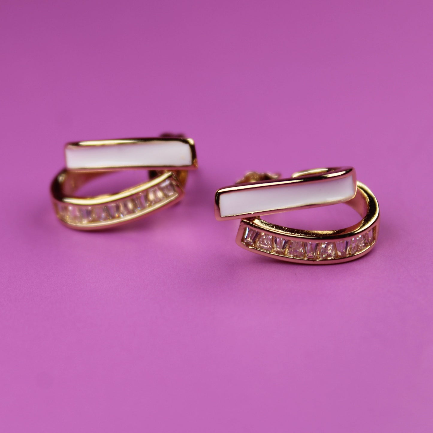 Pair of gold and pink hoop earrings on a pink background