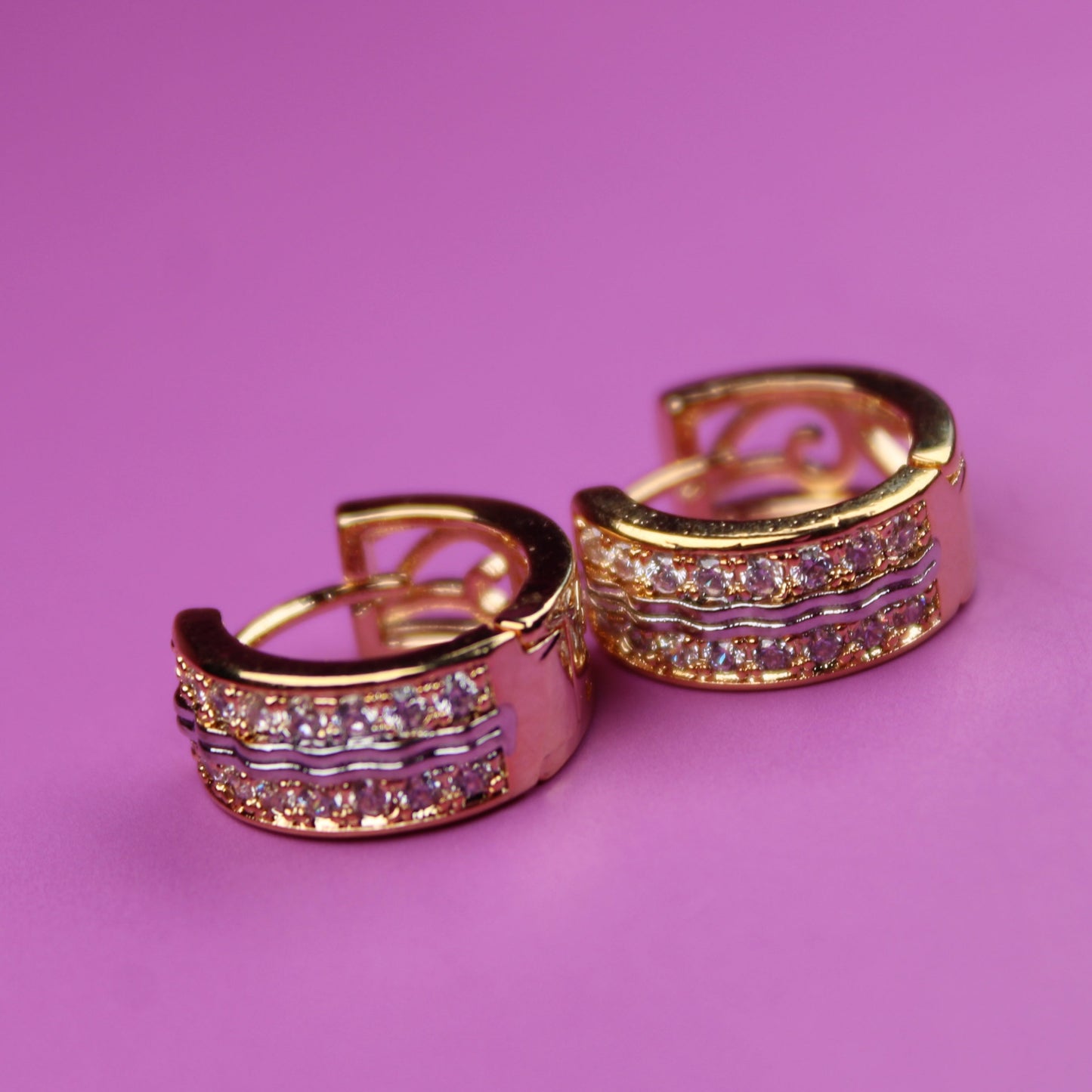 Gold hoop earrings with gemstones on a pink background