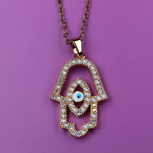 Gold necklace with a hamsa hand pendant on a purple background
